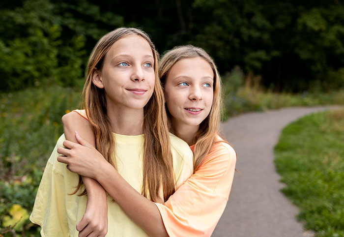 Two identical twin sisters embracing, looking happily into the distance along a winding path. Two identical twin sisters embracing, looking happily into the distance along a winding path.