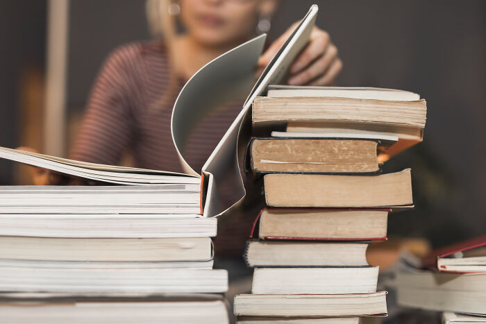 A person with glasses reads among stacks of books, a visual for avoiding corporate buzzwords and practices.