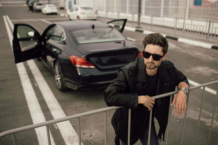 An annoying driver leans on a barrier near his BMW, engaged in a parking war.