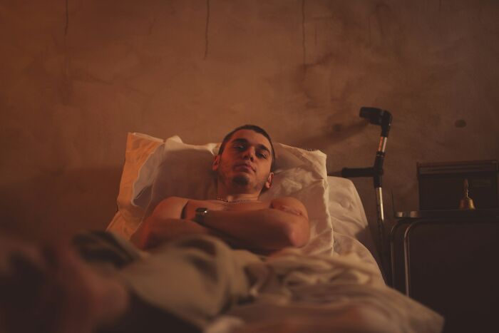 A man lying in bed, arms crossed, with a somber expression, his instincts telling him to get away from creeps.