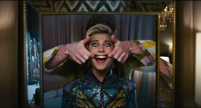 A person behind a woman in a sequined top stretches her face into a wide, forced smile, a scene from terrifying horror movies.