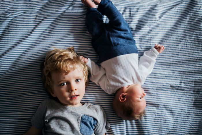 A toddler and a baby lying on a striped bed, representing innocence before realizing they are the problem.