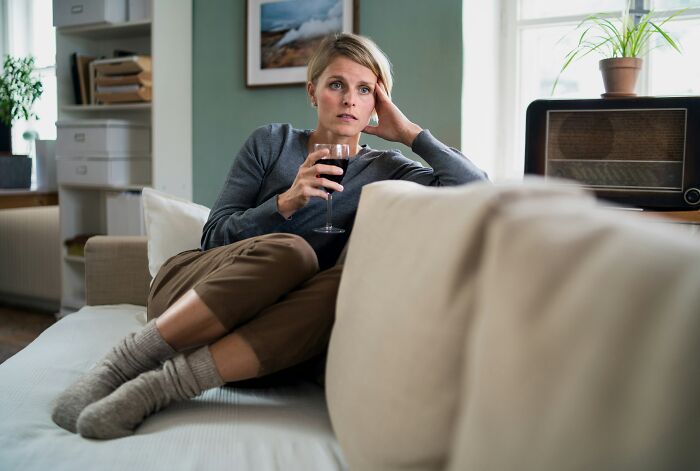 A woman looking worried while holding a glass of wine, pondering moments of realizing she is the problem.