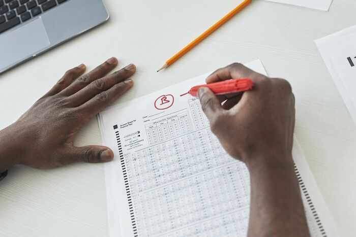 A hand marking a B grade on a test, symbolizing a realization of being the problem.
