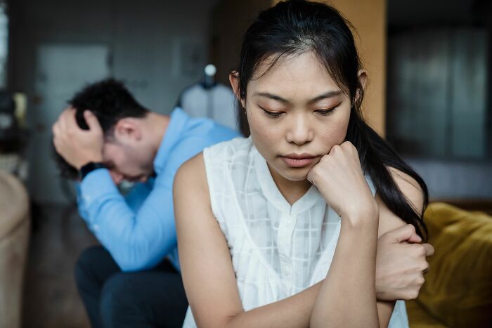 A woman sits in the foreground with a pensive expression, while a man in the background holds his head, realizing he is the problem.