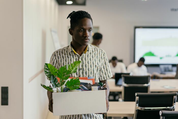 A man carries a box of belongings out of an office, looking downcast, realizing he is the problem.
