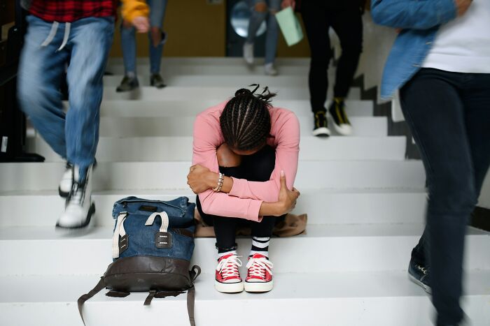 A student sitting alone and dejected on stairs, surrounded by blurred moving students, symbolizing moments people realized they are the problem.