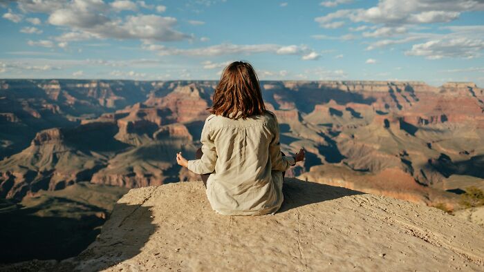 A person meditating on a cliff, realizing they are the problem with the world.