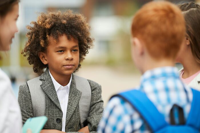 A young boy with curly hair listening intently, possibly realizing that he is the problem in a social interaction.