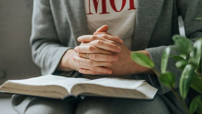 A person with clasped hands over an open book, contemplating self-reflection and realizing the problem.