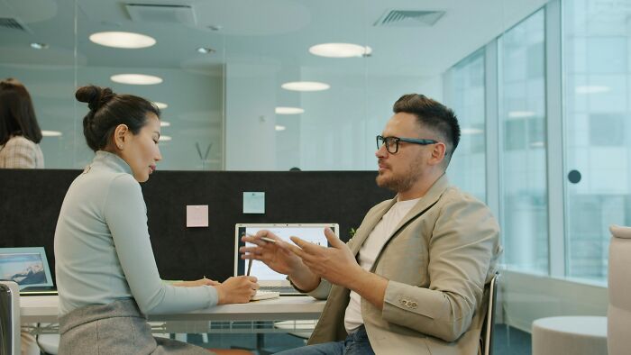 A man gestures while talking to a woman in an office setting, depicting a typical mansplaining scenario.
