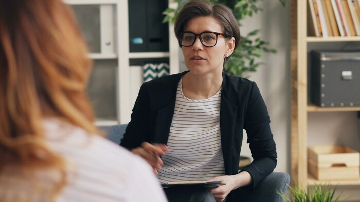 A female therapist with short hair and glasses talking to a client during an unhinged therapist session.