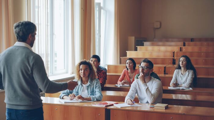 A lecturer teaching students in a tiered classroom, perhaps on topics related to mansplaining examples.