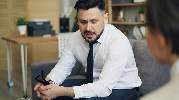 A man in a white shirt and black tie looking distressed, discussing his friend's nanny post.