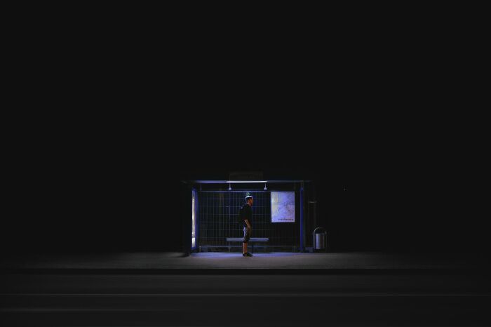 A person standing alone in a disturbing, dark bus stop at night, looking scary.