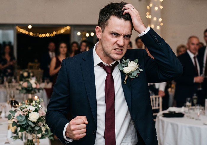 Man at a wedding looking angry and chaotic, with his hand on his head.