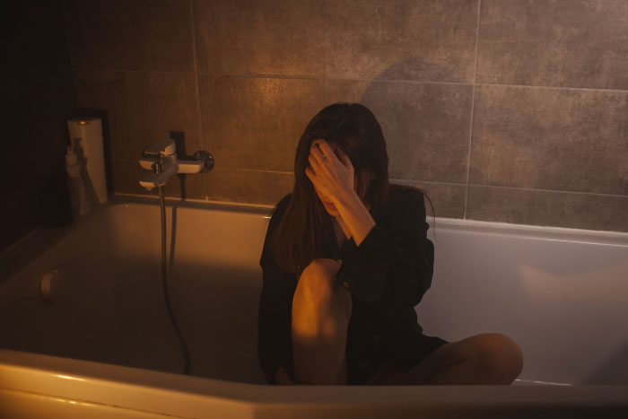 A distressed woman sits in a bathtub, experiencing the worst thing at a wedding.