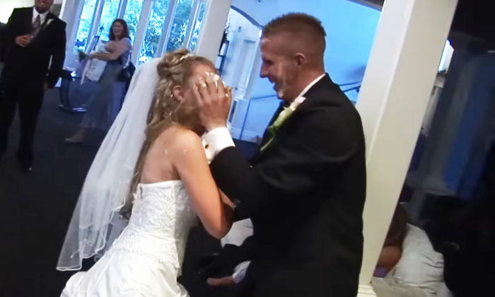 A groom smashes cake into the bride's face at a wedding, illustrating a chaotic moment.