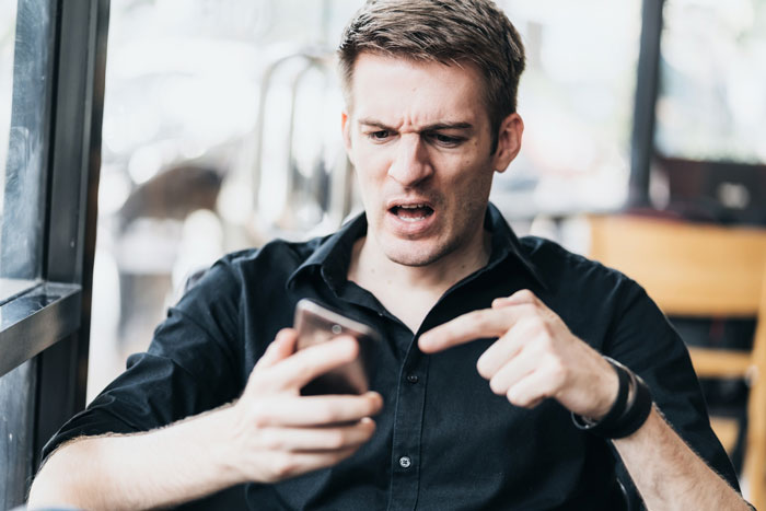 An angry groomsman, looking frustrated, points at his phone after a guy cancels his wedding for another woman. An angry groomsman, looking frustrated, points at his phone after a guy cancels his wedding for another woman.