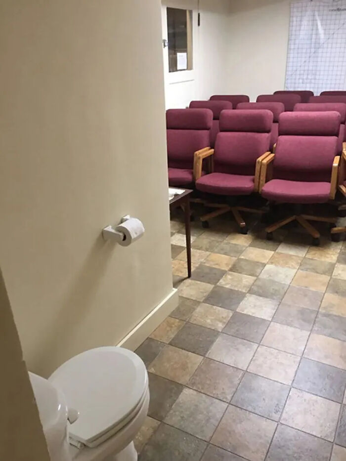 A construction fail: a toilet and toilet paper holder are placed in an open room with chairs, lacking privacy.