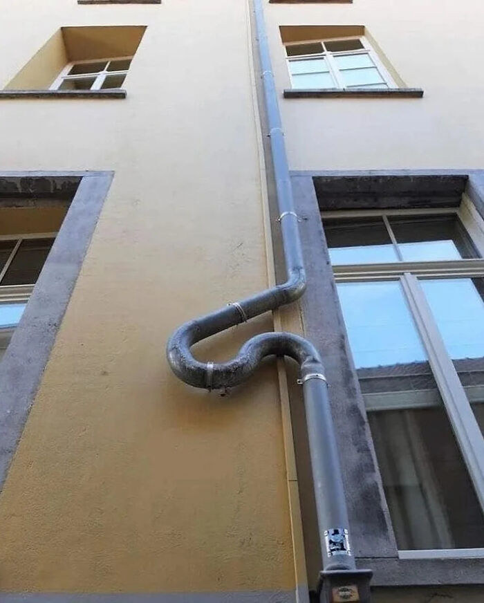 A construction fail with a S-shaped drainpipe on the side of a building, highlighting poor planning. It looks like someone gave up.