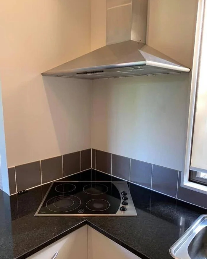 A kitchen construction fail with a stove and range hood awkwardly placed in a corner, illustrating a design flaw.