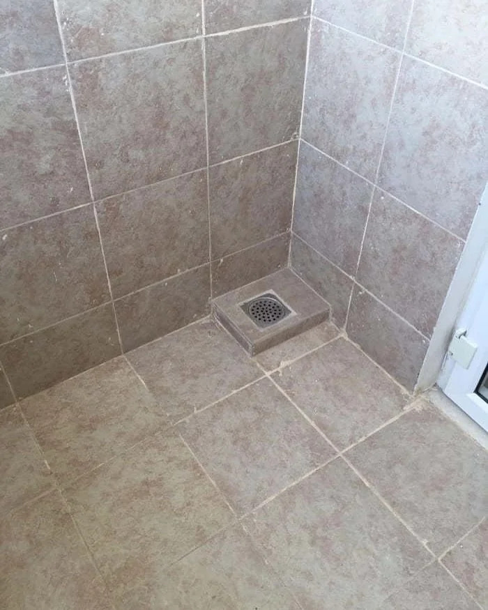 A bathroom construction fail featuring a drain placed in the middle of a tiled floor, not at the lowest point, hindering proper drainage.