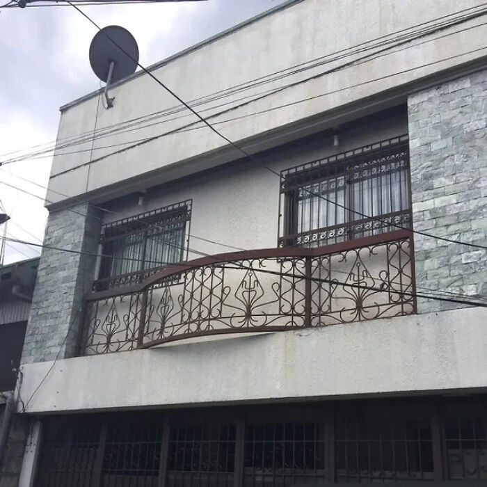 A building with an ornate wrought-iron balcony and satellite dish, showcasing a construction fail in its design.