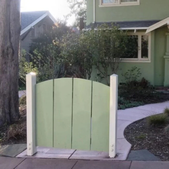 A construction fail: a small, light green wooden fence with no opening stands in front of a walkway.