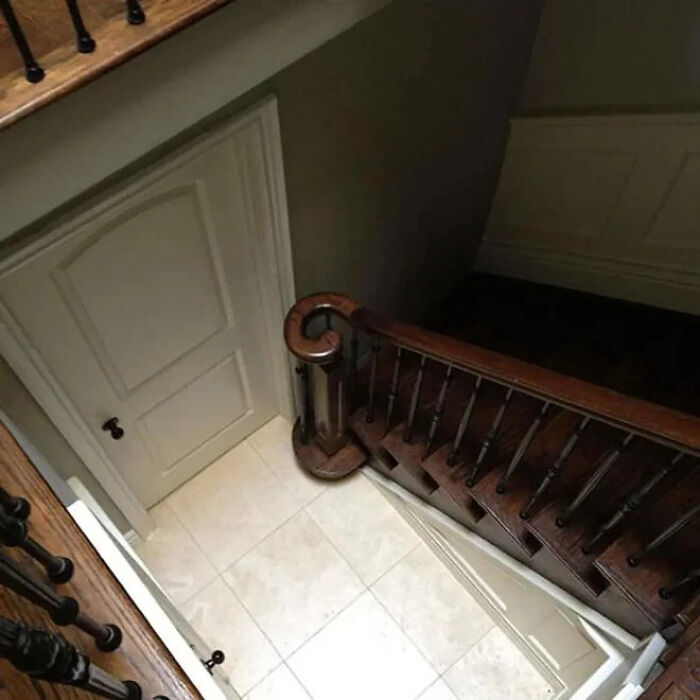 A white door placed directly under a wooden staircase, showcasing construction fails.