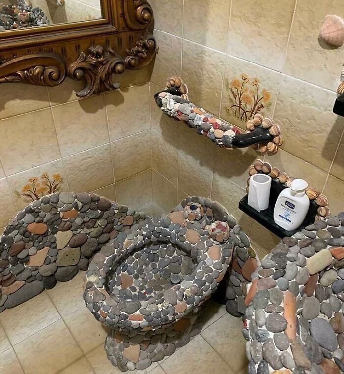 A bathroom with a toilet, sink, and accessories decorated with small rocks, showcasing a construction fail.