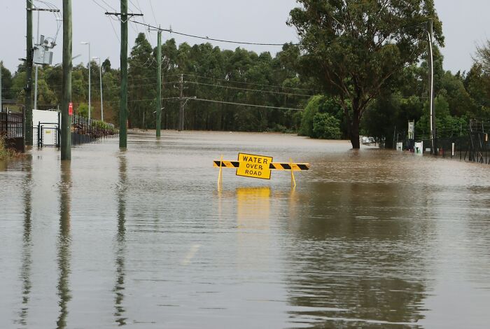 A flooded road with a "water over road" sign, illustrating a terrifying "we need to leave now" moment.