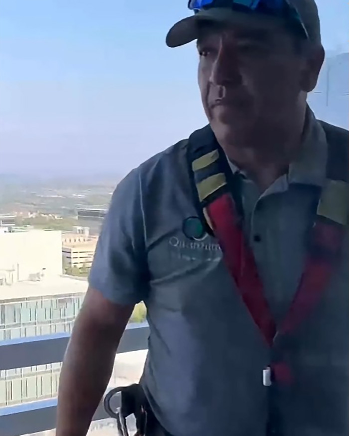 A close-up of a Hispanic window washer in safety gear on a high-rise balcony, looking intently to the side. A close-up of a Hispanic window washer in safety gear on a high-rise balcony, looking intently to the side.