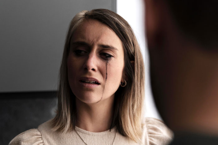 A woman crying with streaks of mascara down her face, showing her husband is horrified as his cancer has no effect on his postpartum wife.