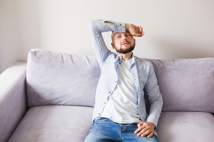 A man looking exhausted on a couch, dealing with cancer and a postpartum wife expecting him to slog at home.