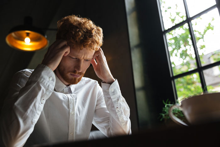 A redhead man looking horrified and stressed, with hands on his head, dealing with cancer news and postpartum wife expectations.
