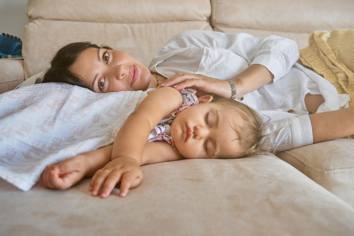 A postpartum wife and her baby resting on a couch, illustrating the challenges of postpartum life and expectations.