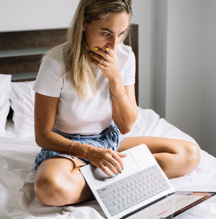 A surprised woman on a bed looking at her laptop, shocked by a plan to make DIL have kids.