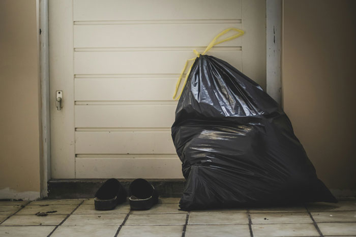A black trash bag and slippers are placed outside a door, representing the discarded plan to have kids and grandbabies.