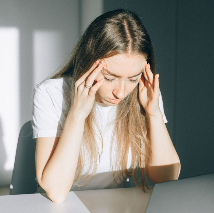 A woman looking stressed, holding her head, connecting the dots about her BF's 10-day trip.