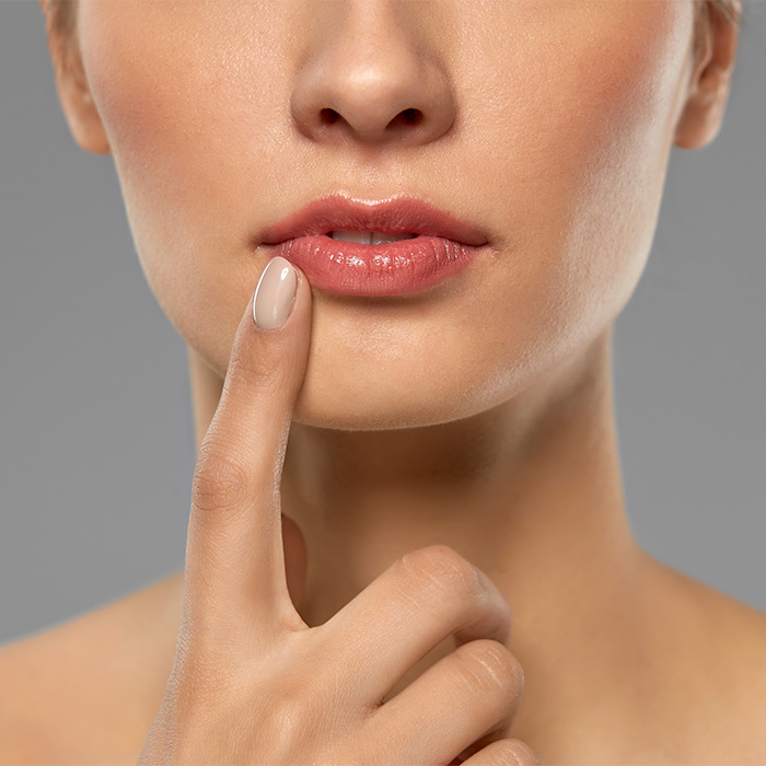 Close-up of a woman's lips, with her finger touching them, showing the potential for cosmetic procedure risks. Close-up of a woman's lips, with her finger touching them, showing the potential for cosmetic procedure risks.