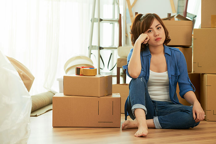 Man hides baby from family, ex tells them. A woman sits on the floor surrounded by moving boxes, looking distraught.