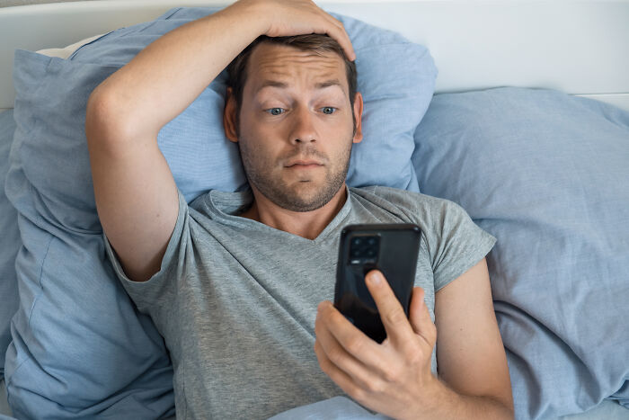 A man in bed looking shocked at his phone, potentially reacting to a request for childcare help. A man in bed looking shocked at his phone, potentially reacting to a request for childcare help.