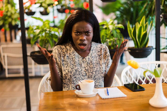 A Black woman looking exasperated in a coffee shop, likely facing a racist Karen over an expensive phone. A Black woman looking exasperated in a coffee shop, likely facing a racist Karen over an expensive phone.