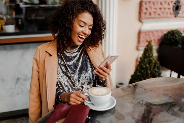 Smiling Black woman using an expensive phone while holding a coffee cup at a cafe, highlighting the 'Racist Karen' incident. Smiling Black woman using an expensive phone while holding a coffee cup at a cafe, highlighting the 'Racist Karen' incident.