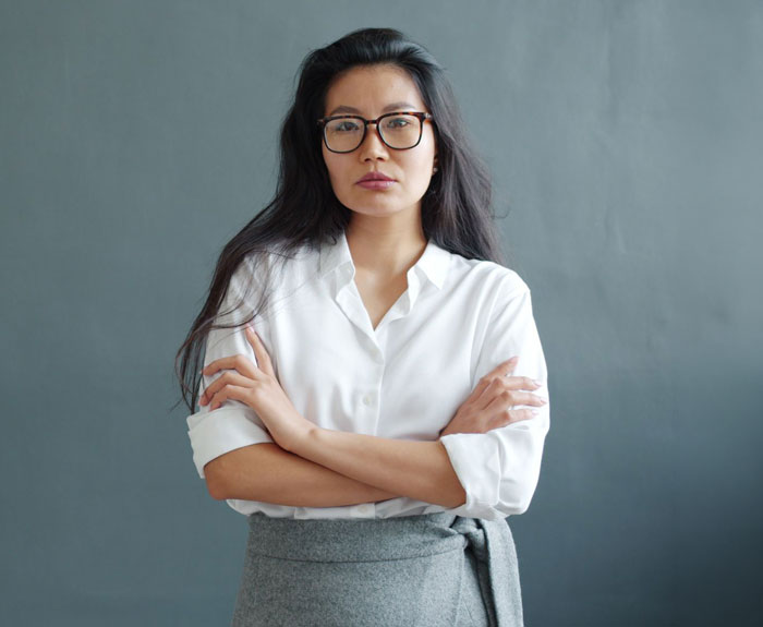 A woman with long dark hair and glasses stands with arms crossed, refusing to eat MILs cooking.