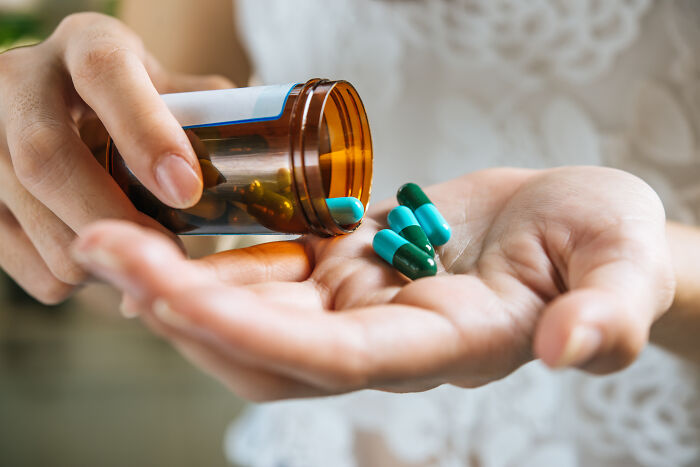 A hand pouring green and blue pills from a bottle, illustrating guests ignoring house etiquette.
