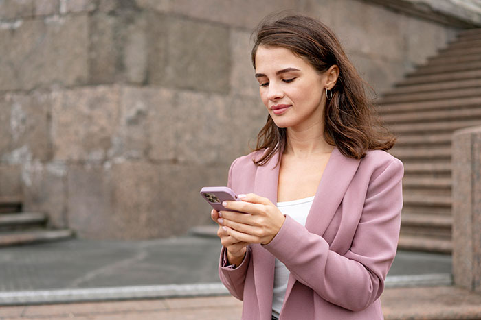 A woman in a pink blazer looks at her phone, representing the bride's conflict with the bridesmaid's BF.
