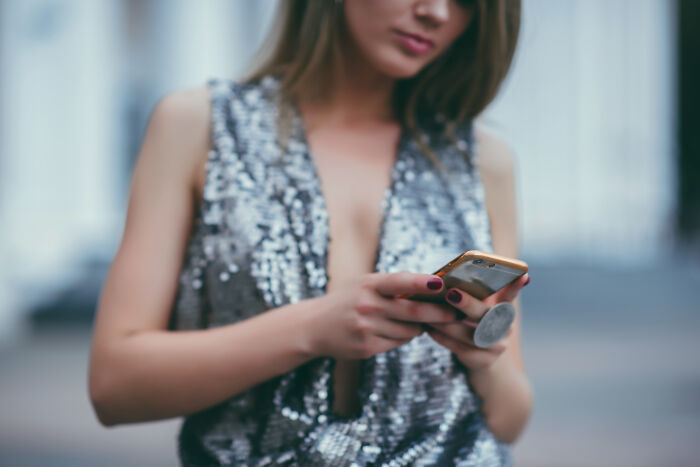 A woman in a sparkly top looking at her phone, representing one of the weddings people regret spending money on.