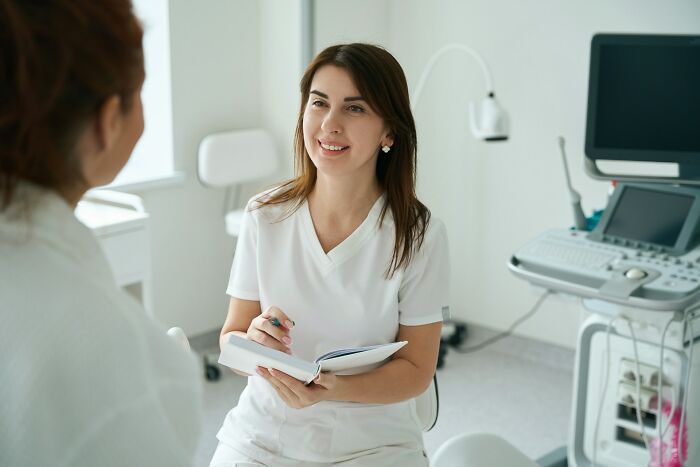 A female gynecologist smiling and taking notes while speaking to a patient about women's health advice.